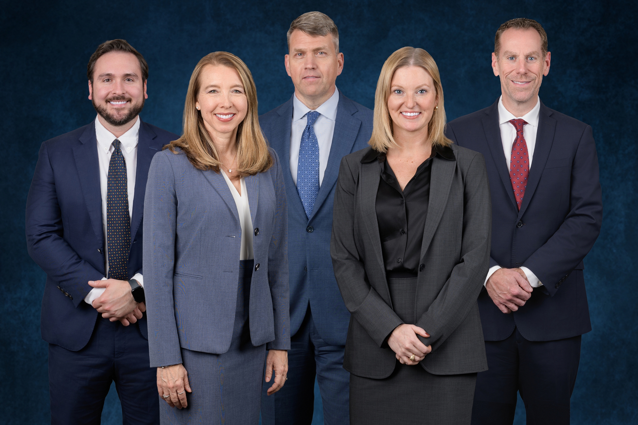 The five attorneys of Rainey & Rainey standing together in suits against a dark blue backdrop